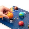 A hand places an orange planet onto a wooden solar system puzzle featuring Mercury, Earth, Venus, Mars, and Jupiter.