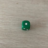 A single green acrylic die with three white dots is placed on a light wooden surface.