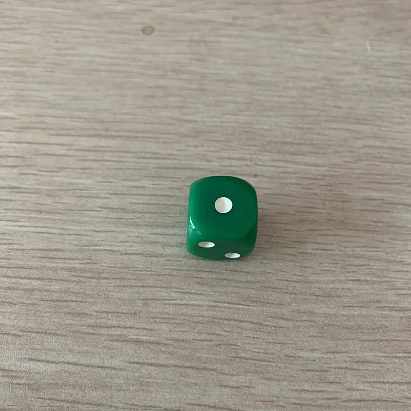 A single green acrylic die with three white dots is placed on a light wooden surface.