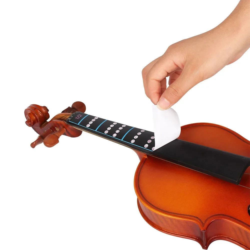 A hand is placing a note sticker onto the fretboard of a violin to demonstrate a beginner's learning tool.