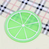 A round, lime green PVC coaster with a sliced fruit pattern rests on a checkered cloth.