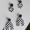 A set of black and white checkered polymer clay earrings with a floral stud design.