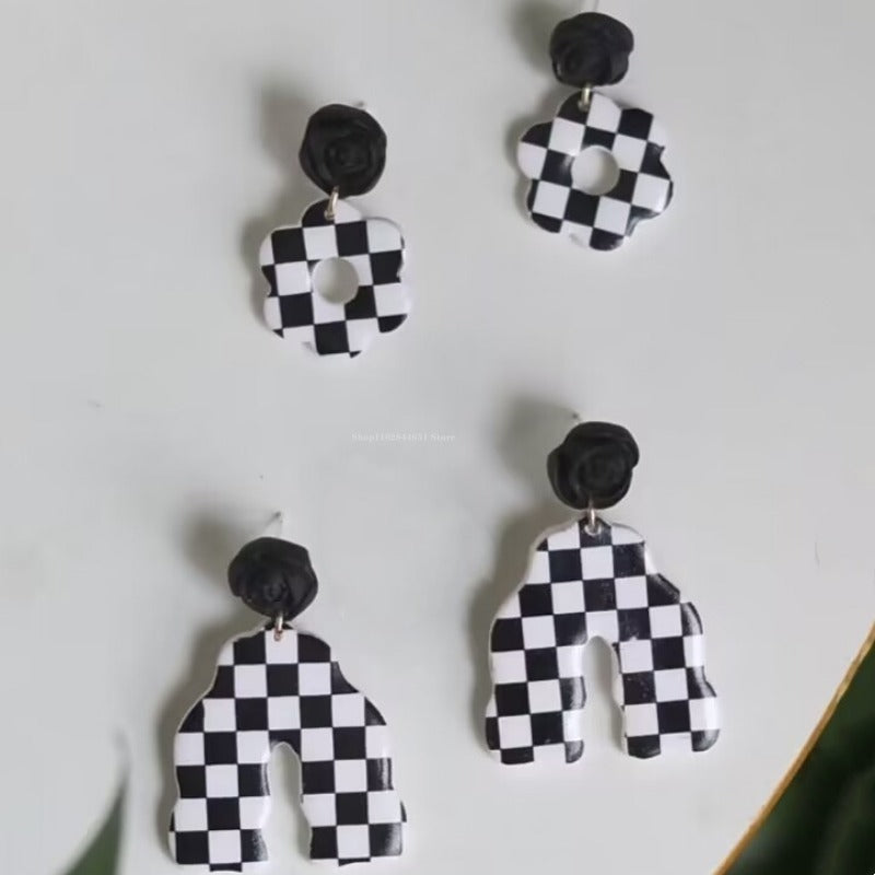 A set of black and white checkered polymer clay earrings with a floral stud design.