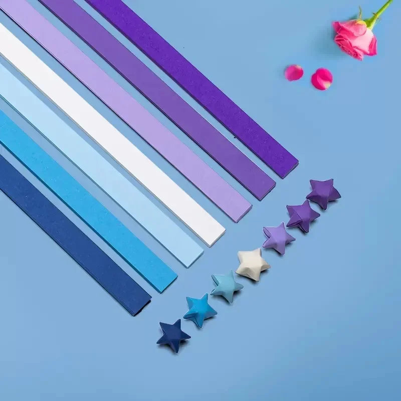 A collection of 27 assorted colored origami star strips laid diagonally on a blue background with pink flowers.