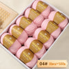 Box of Merino wool yarn balls in pink and gold labels, packaged for knitting projects.