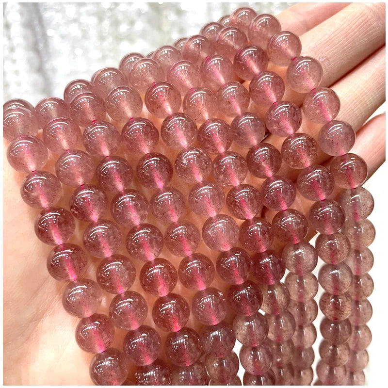 A hand holds a strand of pinkish-red natural stone beads for DIY jewelry making