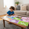 A young boy is crafting with a geometric animal sticker book on a wooden table in a bright living room.