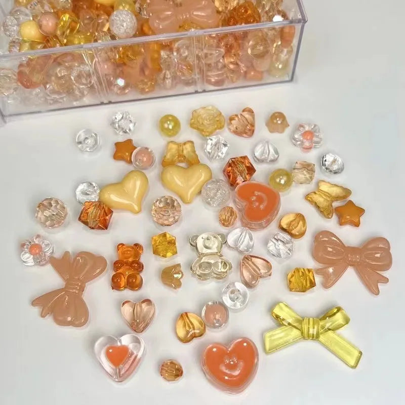 A collection of mixed acrylic bow and flower beads in various shades of orange, yellow, and clear are displayed on a white su