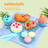 A tablecloth is set with a pretend play picnic and tea party arrangement featuring food items like bread, donuts, and macaron