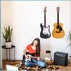 A person is playing a white guitar in front of a wall display featuring several guitars mounted on wood panels.