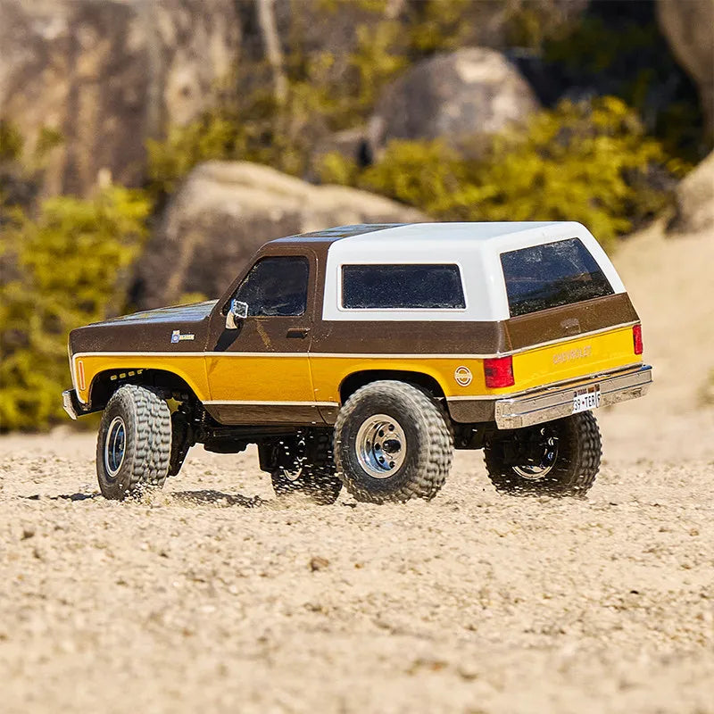 A brown and white 1:24 scale Chevrolet K5 Blazer RC crawler vehicle on a sandy terrain.