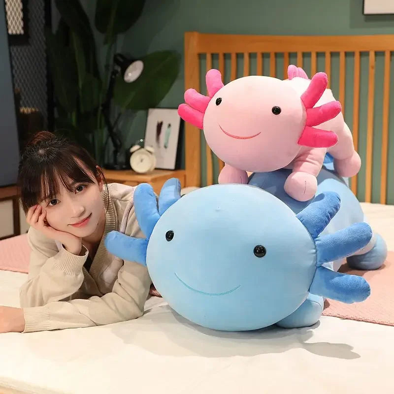 A person is leaning on a large blue axolotl plush pillow, with a pink axolotl plush resting beside it.