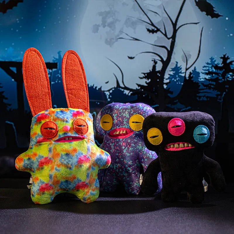 A colorful monster plush doll with orange ears sits in front of a dark background featuring a moon and silhouetted trees.