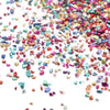 A close-up of multicolored crushed glass stones in various shades of pink, blue, and gold scattered on a white surface.
