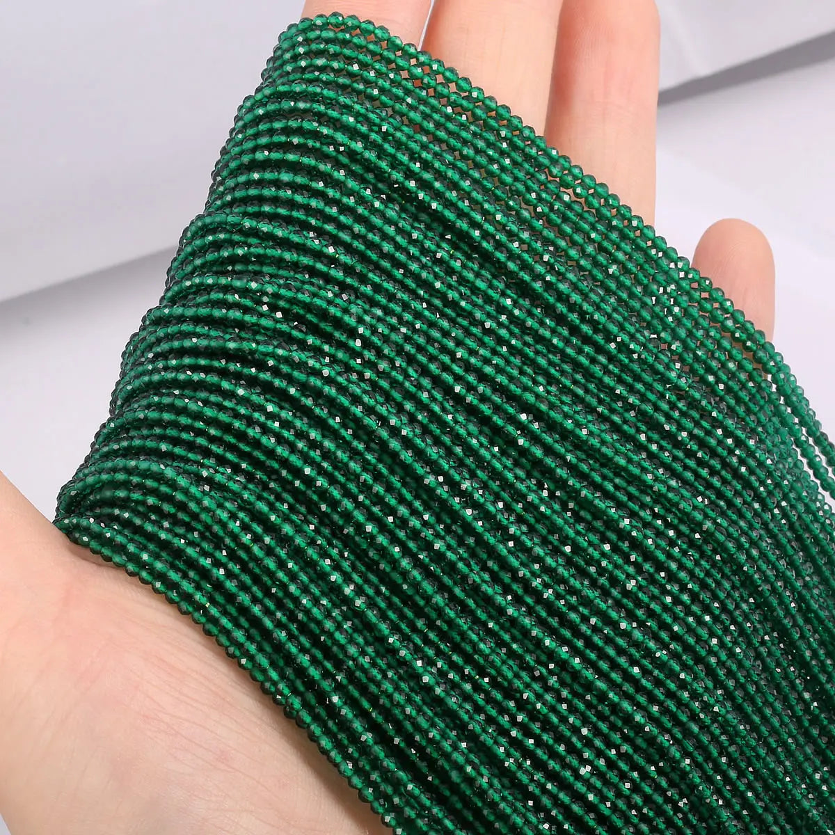 A close-up of a green beaded bracelet made from faceted natural stone beads being worn on a hand.