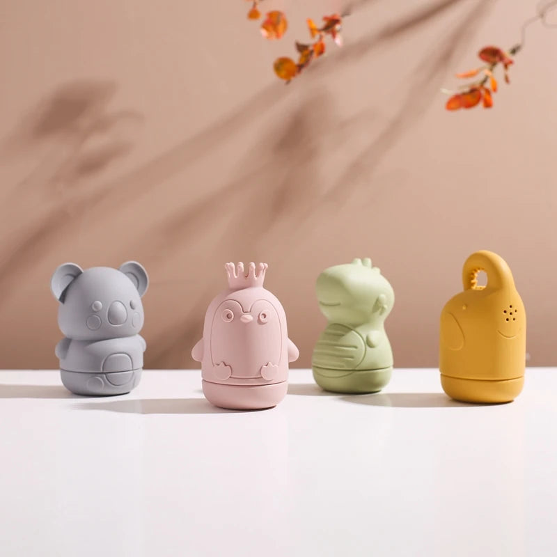 A collection of soft silicone animal bath toys in gray, pink, green, and yellow sitting on a white surface.