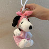 A white Snoopy plush toy with a pink and white striped bow and outfit is being held by a hand.