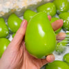 A hand holds a bright green color-changing mango squishy stress ball against a clear background.