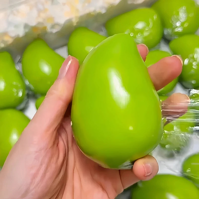 A hand holds a bright green color-changing mango squishy stress ball against a clear background.