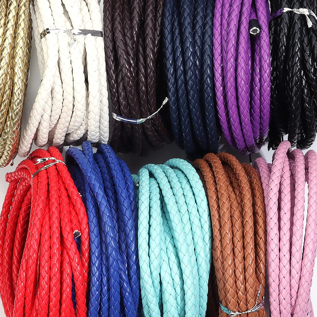 A collection of round braided leather cords in various colors including gold, white, black, purple, blue, red, and pink.
