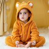 A baby wearing an adorable orange hooded romper resembling a fox, sitting on a white fluffy surface.