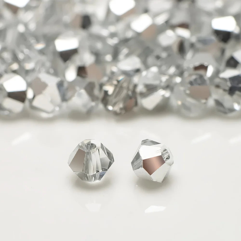 A close-up of faceted, clear and silver crystal beads scattered on a white surface.