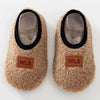 Pair of beige fuzzy baby slippers with black trim and clear plastic soles.