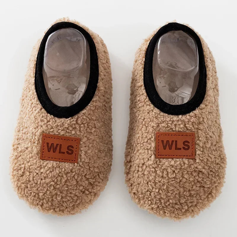 Pair of beige fuzzy baby slippers with black trim and clear plastic soles.