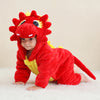A baby wearing a red and yellow hooded dinosaur romper with a fierce face design.