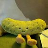 A soft, yellow pickle-shaped plush toy with small eyes and stubby legs sitting on a green surface.