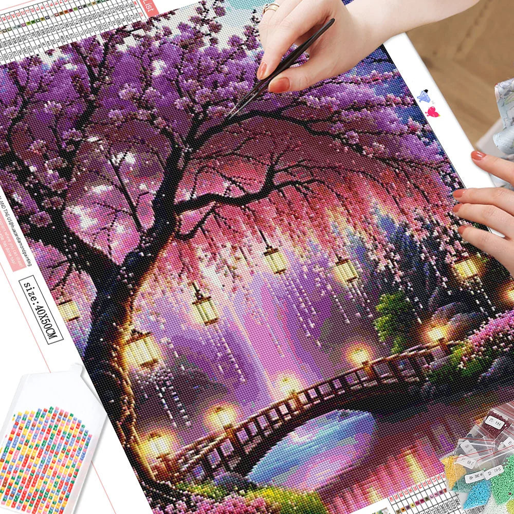 A diamond painting kit featuring a vibrant landscape of a flowering tree, glowing lanterns, and a bridge at night.