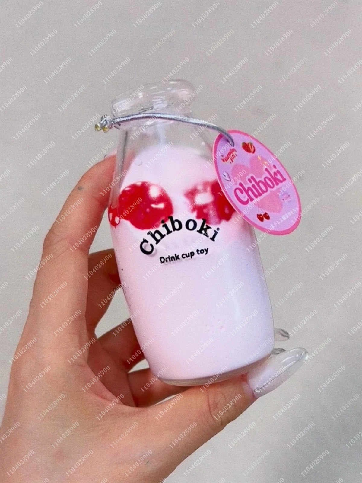 A hand holds a pink glass bottle filled with liquid and red squishy toys labeled Chiboki Drink cup toy