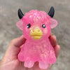 A hand holds a pink glitter highland cow squishy stress relief toy.