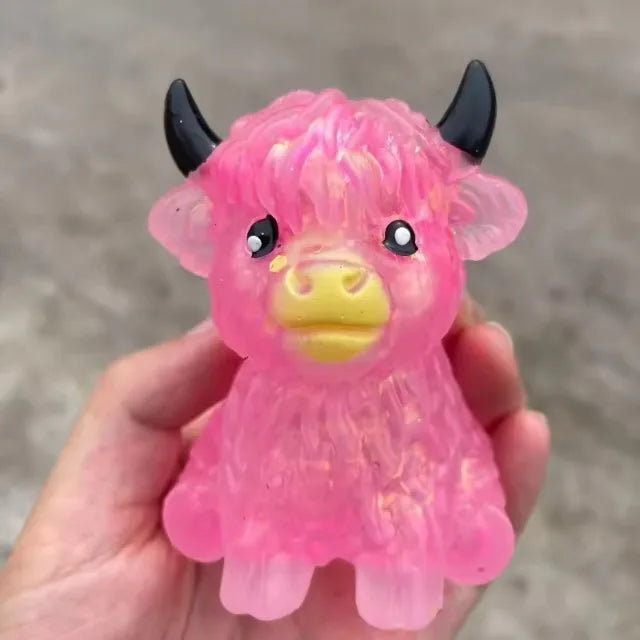 A hand holds a pink glitter highland cow squishy stress relief toy.