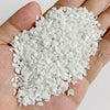 A hand holds a pile of white tumbled stone chips for jewelry making and home decor.