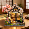A detailed miniature Japanese tea house diorama featuring pink blossoms and traditional architecture.