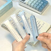 A hand holds a light blue adhesive dot tape glue roller next to a spiral notebook and a calculator.