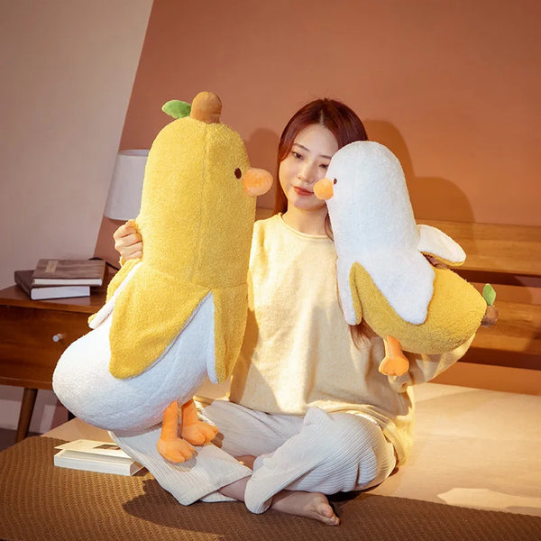 A woman is sitting on the floor surrounded by a yellow and white banana duck plush pillow.