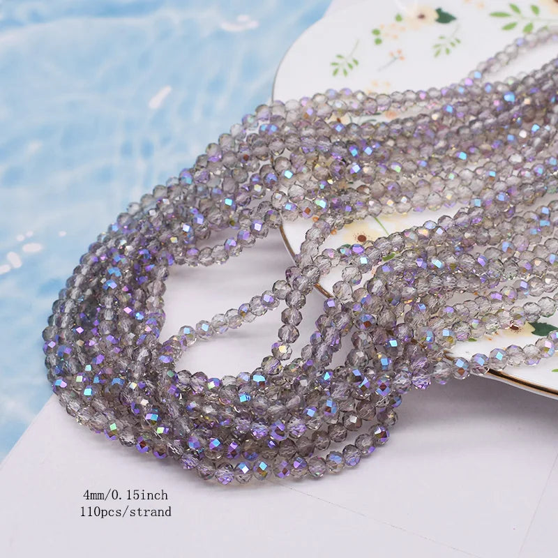 A strand of faceted purple and gray crystal rondelle beads for jewelry making laid on a white surface.