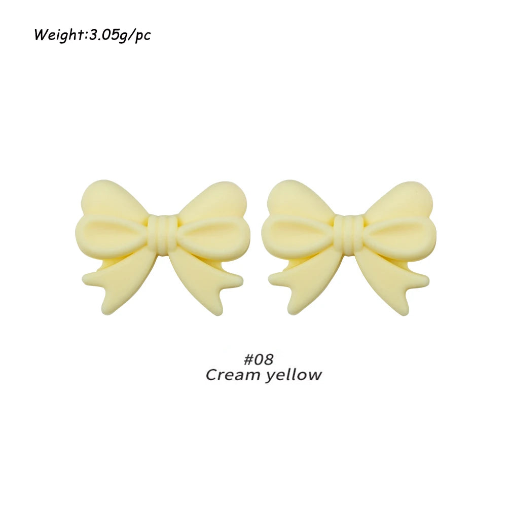 A pair of pale yellow silicone bow tie beads used for jewelry making and craft projects.