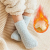 A pair of light blue fuzzy fleece socks resting on a beige knitted surface with a glowing orange flame.