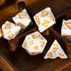 A set of seven white and orange polyhedral dice resting in a wooden box.