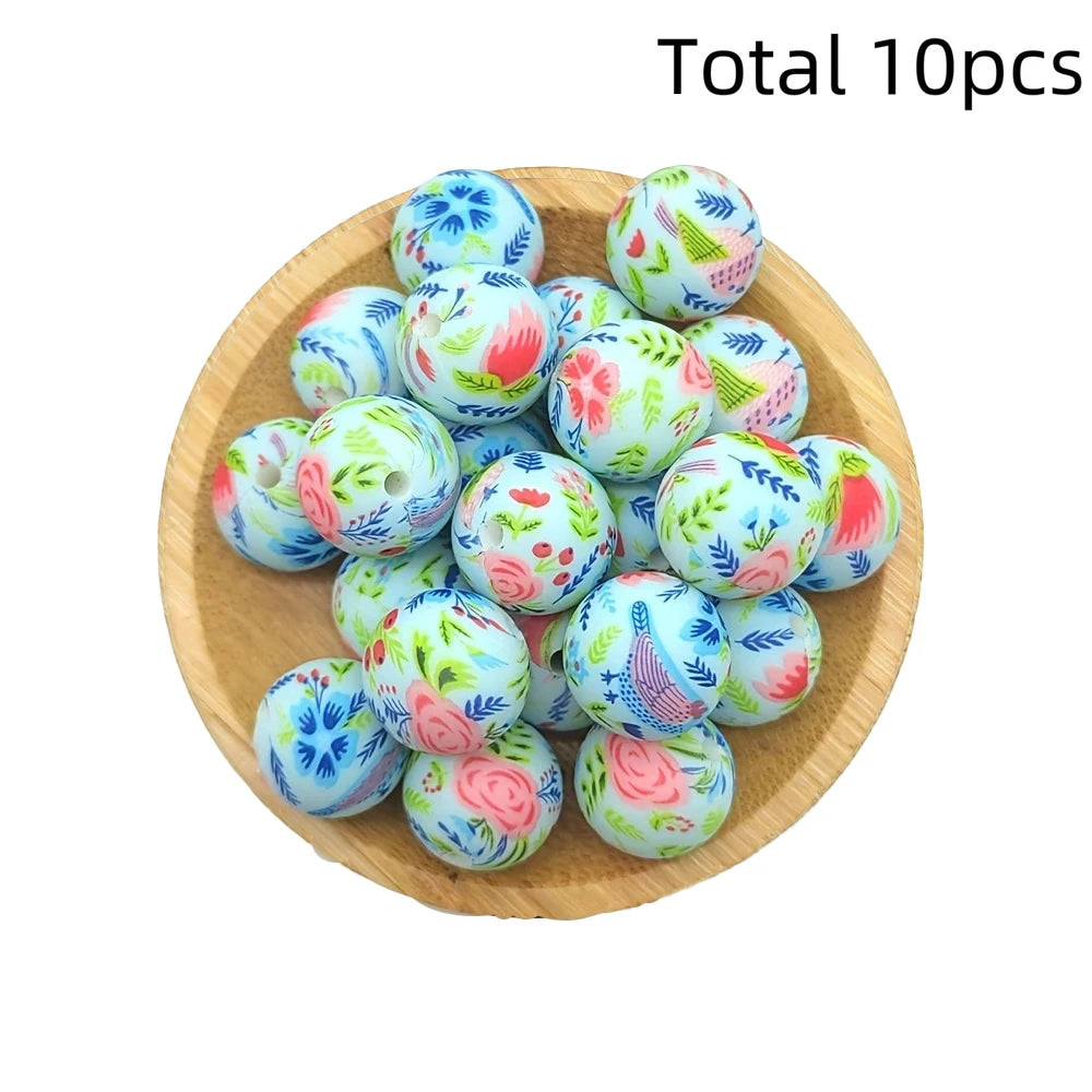A collection of ten colorful printed silicone beads in various floral patterns arranged on a wooden surface.