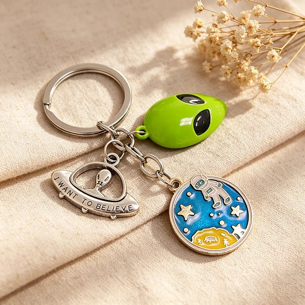 A silver key chain featuring a green astronaut mask charm and a blue celestial design.