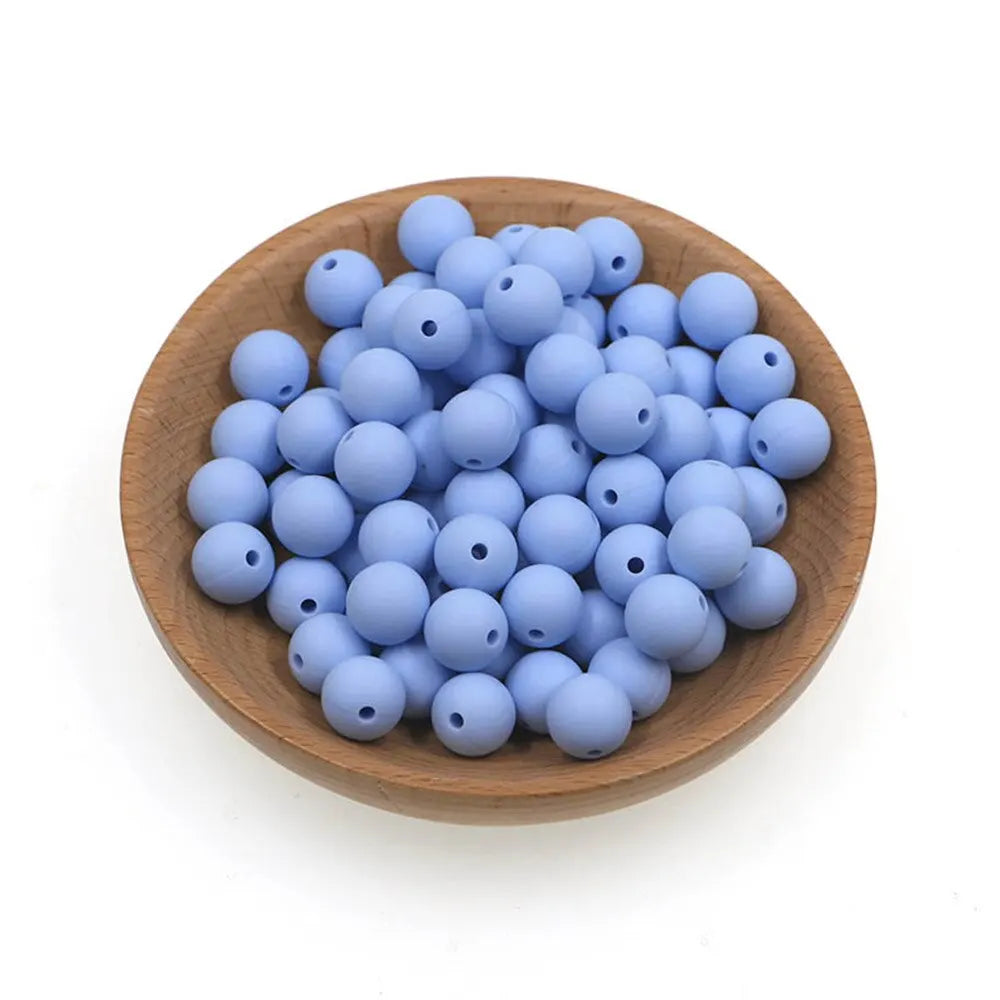 A pile of small, round, light blue silicone beads in a wooden bowl for jewelry making.