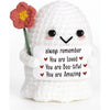 A white crochet ghost doll with a pink flower on its head holding an emotional support card that says You are loved you are b
