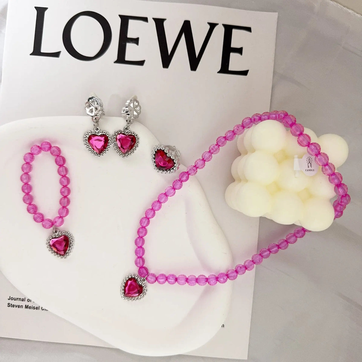 A set of pink and clear gemstone jewelry including earrings, a necklace, and a charm, displayed on a white surface.