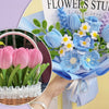 Un bouquet de fleurs bleues dans un papier bleu à côté d'un panier de tulipes roses.
