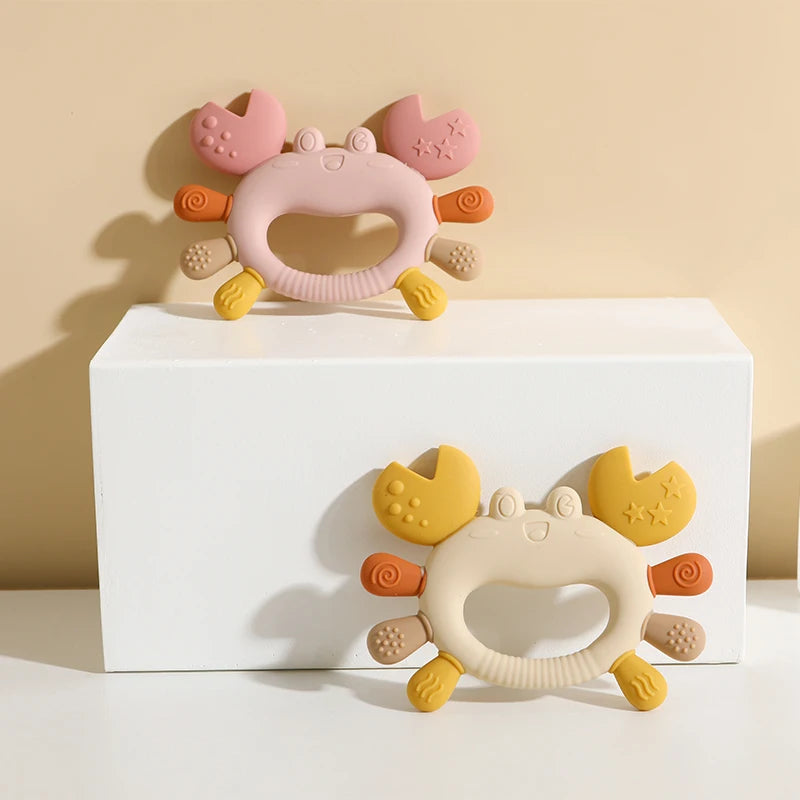 A silicone baby teether shaped like a crab, featuring pink and yellow components.