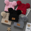 A collection of pink, red, and gray knit baby beanie hats with fluffy pom-poms displayed on a gray background.
